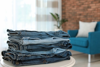 Photo of Stack of stylish jeans on table against blurred background