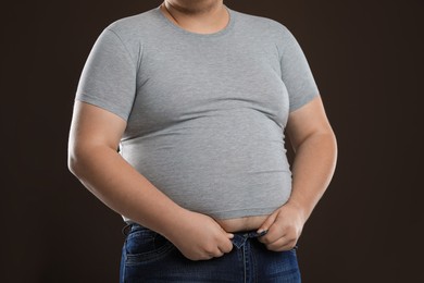 Overweight man trying to button up tight jeans on dark brown background, closeup