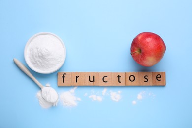 Photo of Word Fructose made of wooden cubes, powder and fresh apple on light blue background, flat lay