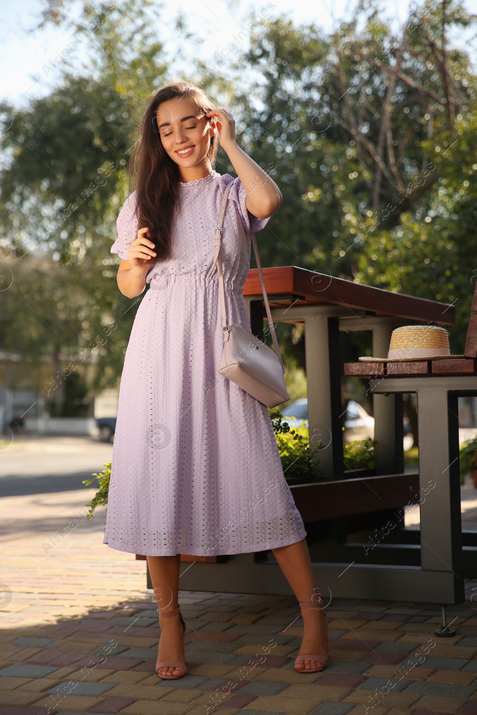 Photo of Beautiful young woman in stylish violet dress with handbag outdoors