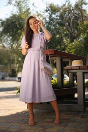 Photo of Beautiful young woman in stylish violet dress with handbag outdoors