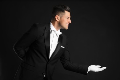 Handsome butler in elegant uniform on black background