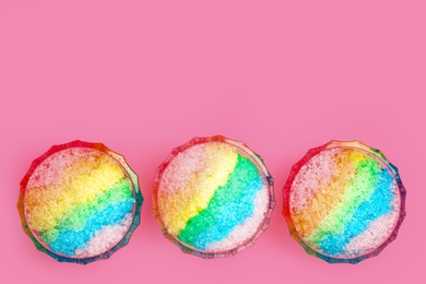 Photo of Rainbow shaving ice in glass dessert bowls on pink background, flat lay. Space for text