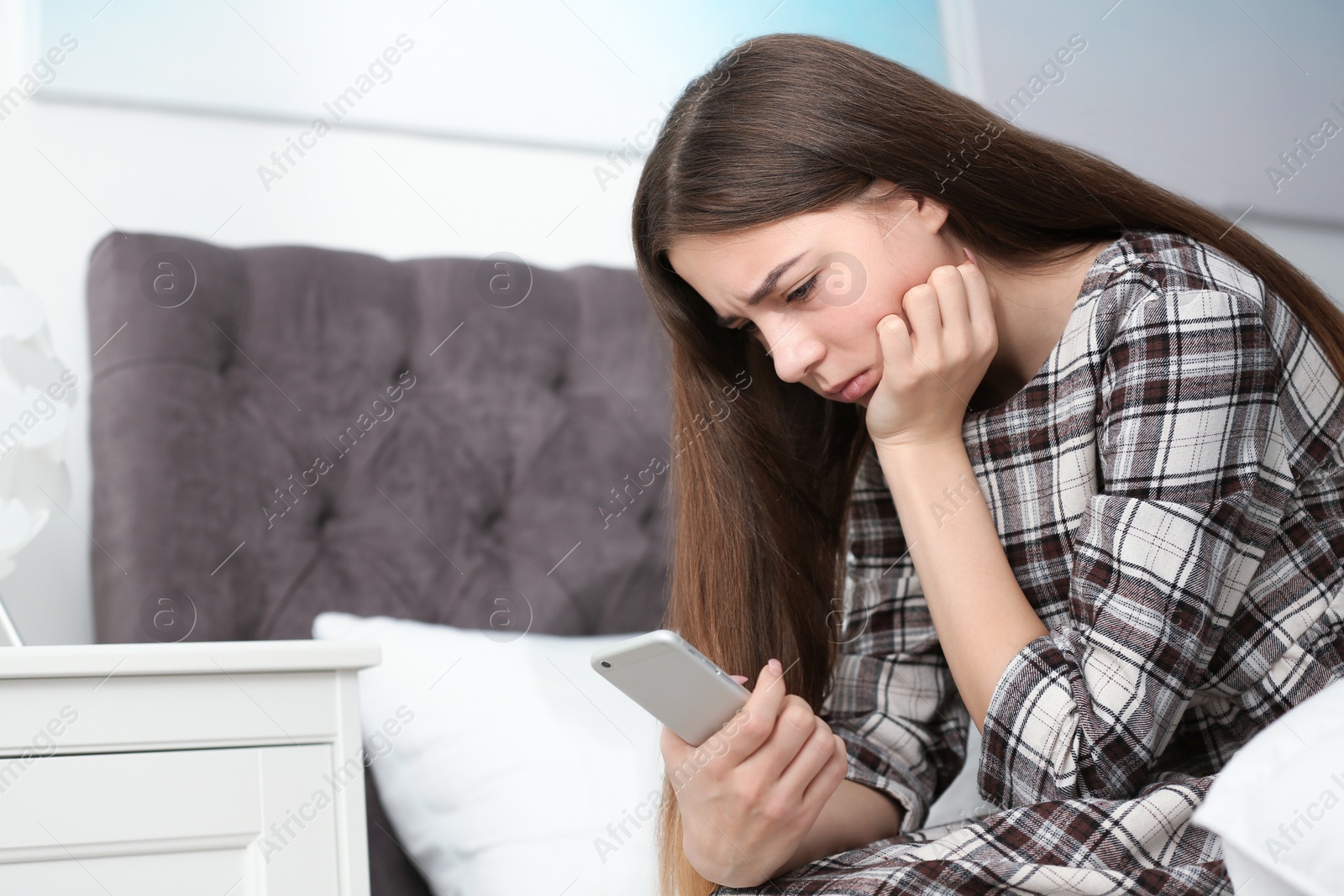 Photo of Upset teenage girl with smartphone sitting on bed. Space for text