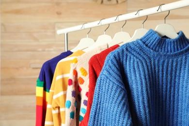 Photo of Collection of warm sweaters hanging on rack against wooden background