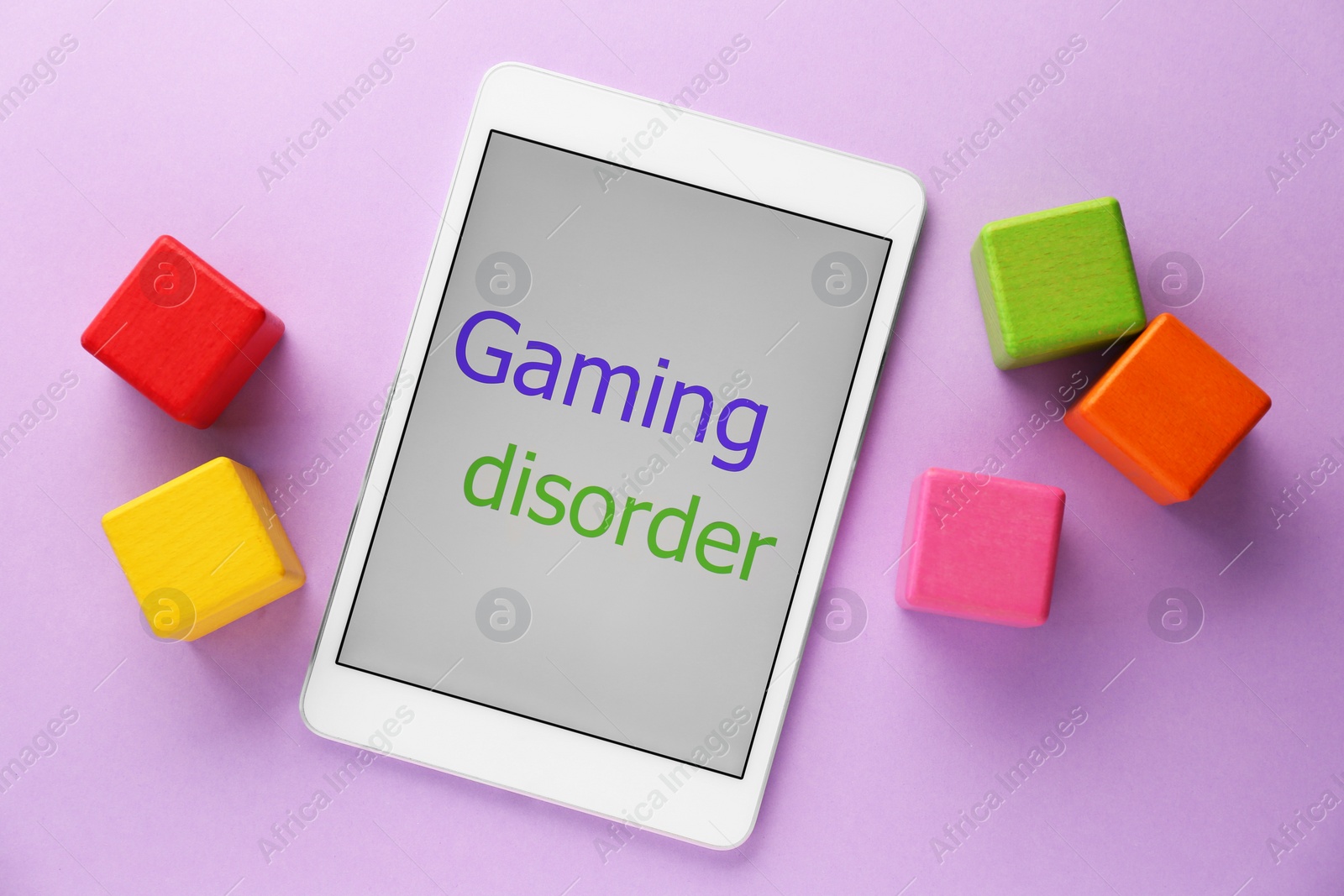 Photo of Tablet with phrase Gaming Disorder and colorful cubes on violet background, flat lay. Addictive behavior