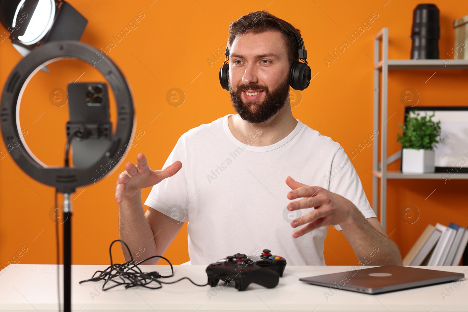 Photo of Smiling technology blogger with game controllers explaining something while recording video at home