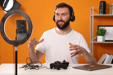 Smiling technology blogger with game controllers explaining something while recording video at home