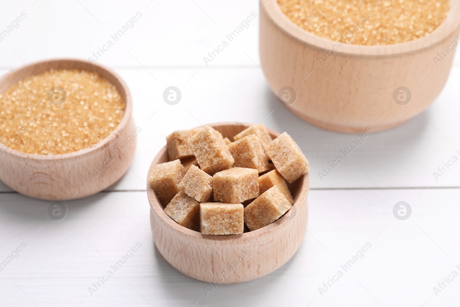 Photo of Different types of brown sugar in bowls on white wooden table, closeup