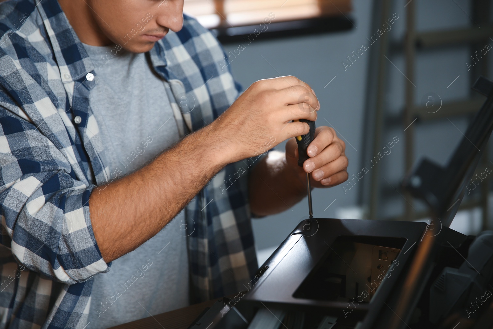 Photo of Repairman with screwdriver fixing modern printer indoors, closeup