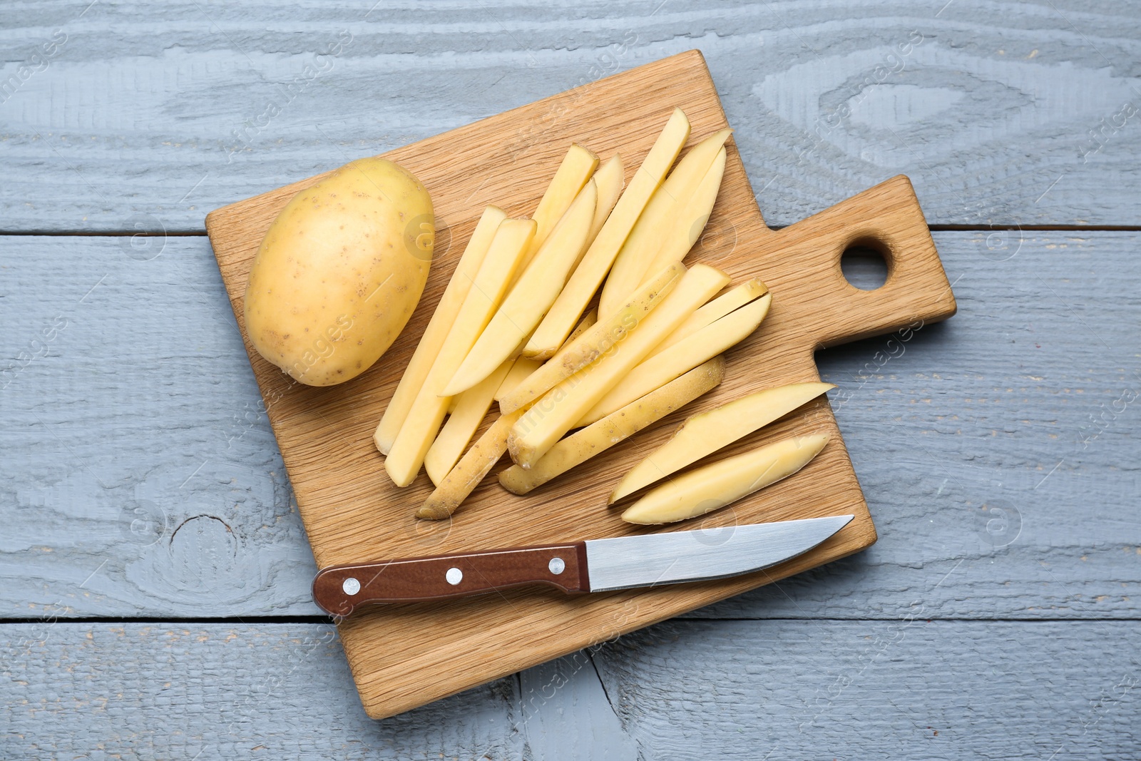 Photo of Whole and cut potatoes with knife on grey wooden table, top view. Cooking delicious french fries