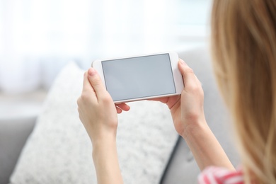 Young woman using video chat on smartphone in living room, closeup. Space for design