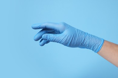 Doctor wearing medical glove on light blue background, closeup