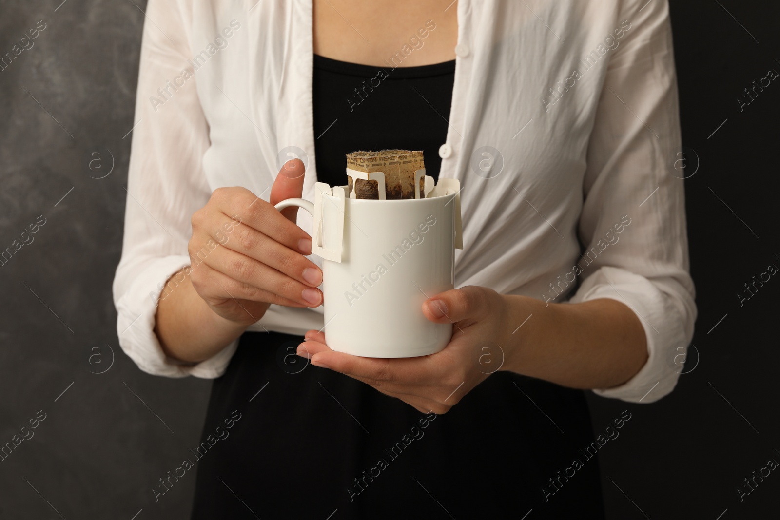 Photo of Woman holding cup with drip coffee bag on grey background, closeup