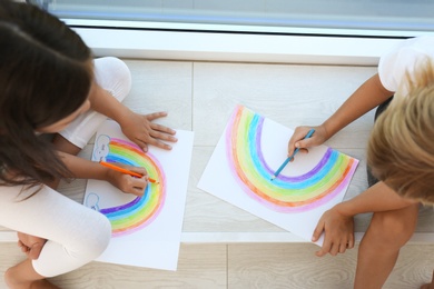 Photo of Little children drawing rainbows indoors, above view. Stay at home concept