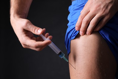 Man injecting himself on black background, closeup. Doping concept