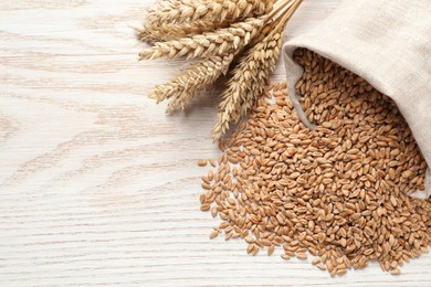 Photo of Wheat grains and spikes on white wooden table, flat lay. Space for text
