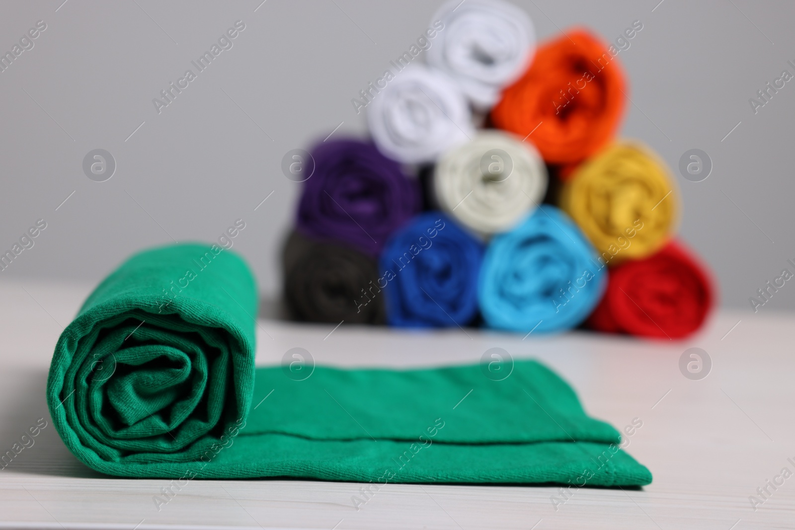 Photo of Sorting and organizing. Different rolled clothes on white wooden table, closeup