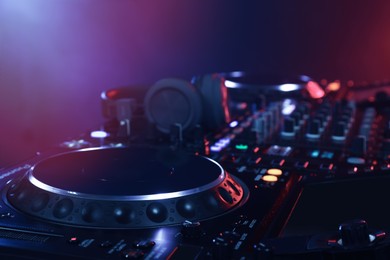 Photo of Closeup view of modern DJ controller with headphones on color background