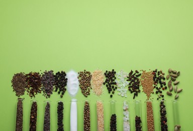 Photo of Test tubes with various spices on green background, flat lay. Space for text
