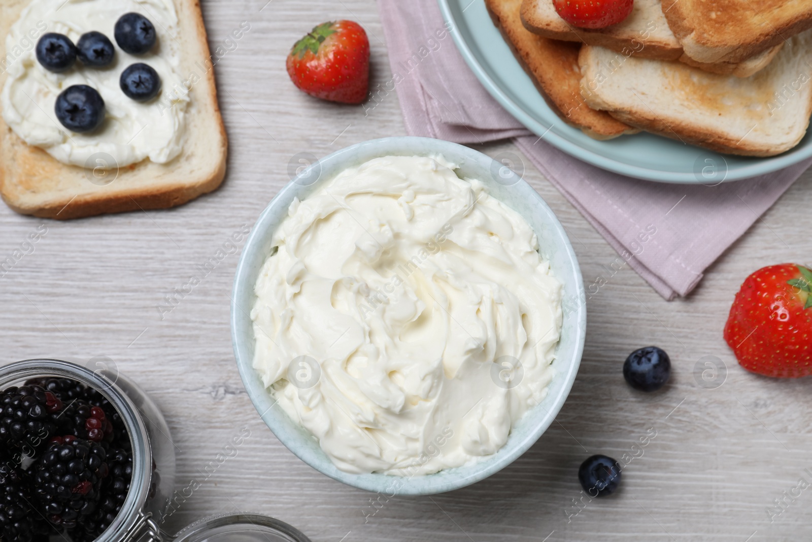 Photo of Tasty cream cheese, toasted bread and fresh berries on white wooden table, flat lay