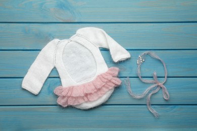 Photo of Knitted baby girl bodysuit and headband with beads on light blue wooden background, flat lay. Cute outfit for photoshoot