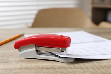 Photo of Bright stapler with documents on wooden table indoors, closeup