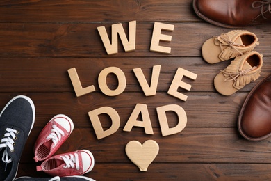Photo of Flat lay composition with shoes and words WE LOVE DAD on wooden background. Father's day celebration