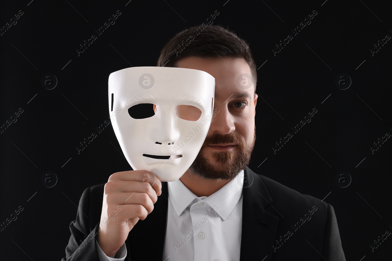 Photo of Multiple personality concept. Man covering face with mask on black background