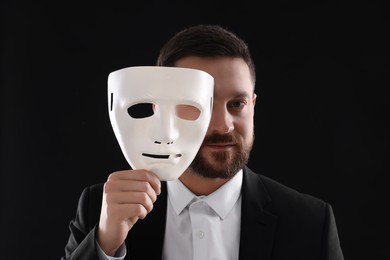 Multiple personality concept. Man covering face with mask on black background