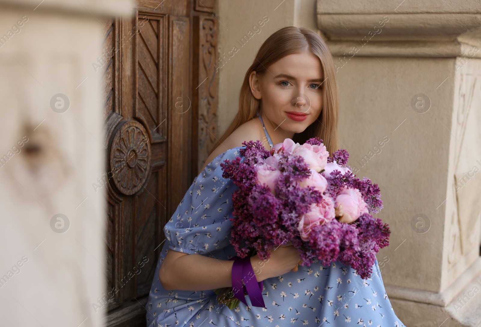 Photo of Beautiful woman with bouquet of spring flowers near building outdoors