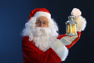 Photo of Santa Claus holding Christmas lantern with burning candle on dark blue background