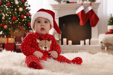 Photo of Baby in Santa hat and bright Christmas pajamas on floor at home