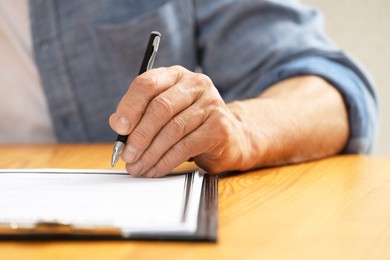 Senior man signing Last Will and Testament at wooden table, closeup