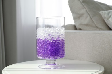 Photo of Different color fillers in glass vase on white table at home. Water beads