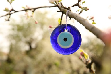 Photo of Evil eye amulet hanging on blossoming spring tree outdoors, closeup. Space for text