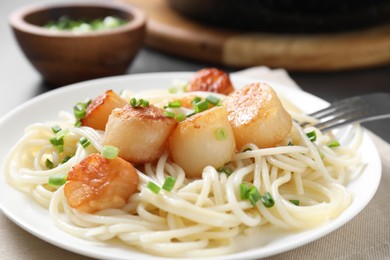 Photo of Delicious scallop pasta with green onion served on grey table, closeup