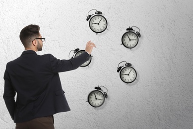Image of Time management concept. Businessman stretching hand to falling alarm clocks on light background
