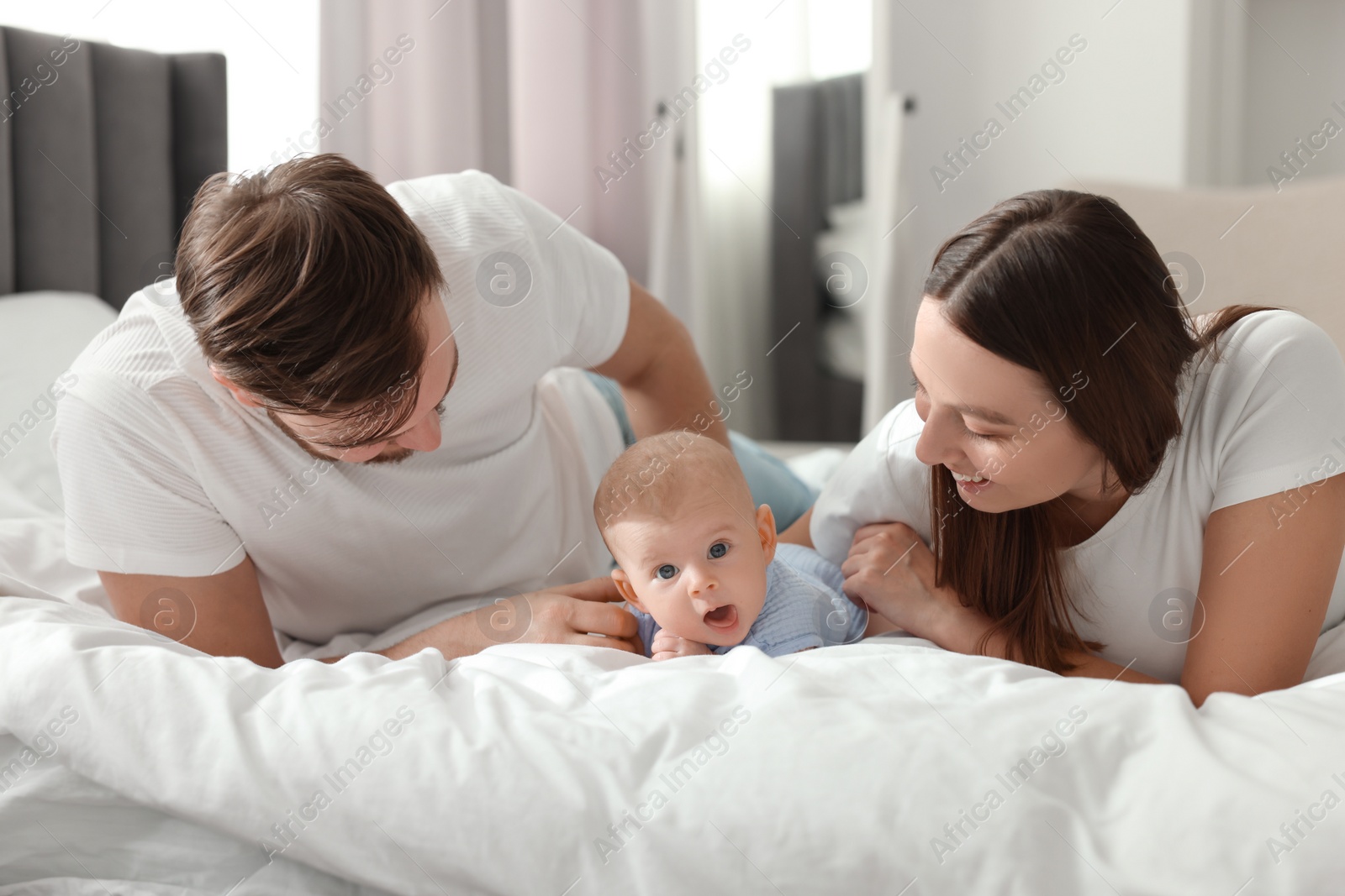 Photo of Happy family. Parents with their cute baby on bed indoors