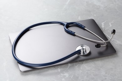 Modern laptop and stethoscope on grey table