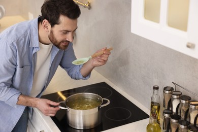 Man tasting delicious chicken soup in kitchen