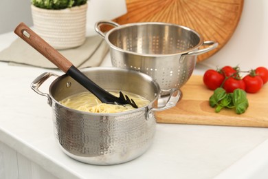 Photo of Cooked spaghetti and pasta server in metal pot on white countertop