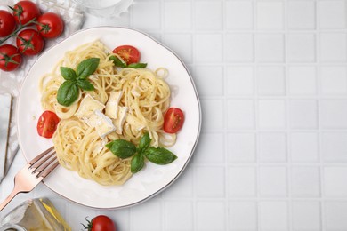 Photo of Delicious pasta with brie cheese, tomatoes and basil leaves served on white tiled table, flat lay. Space for text