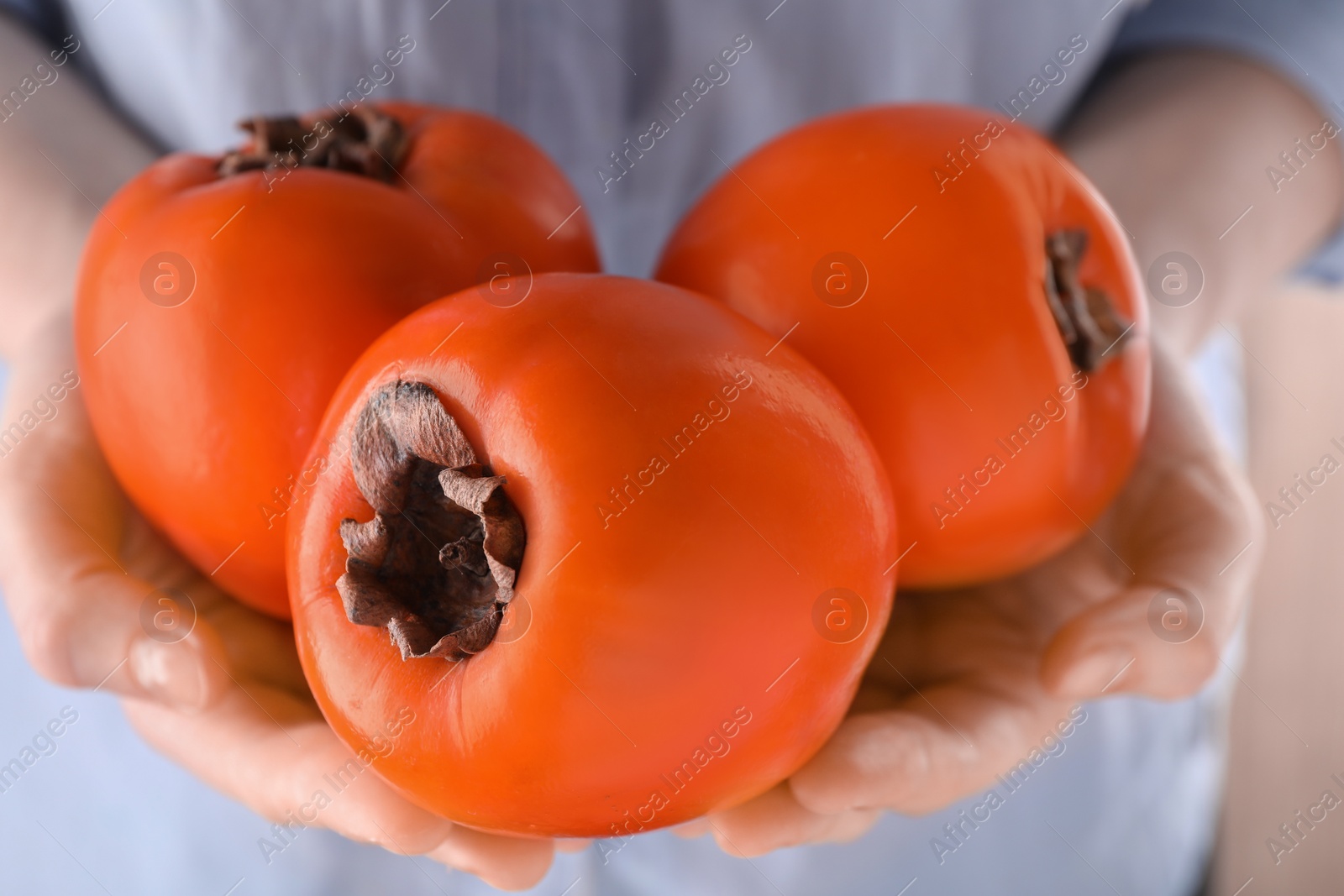 Photo of Woman holding delicious ripe juicy persimmons on blurred background, closeup