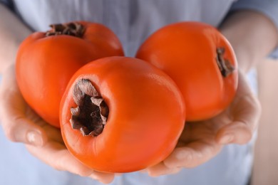 Woman holding delicious ripe juicy persimmons on blurred background, closeup