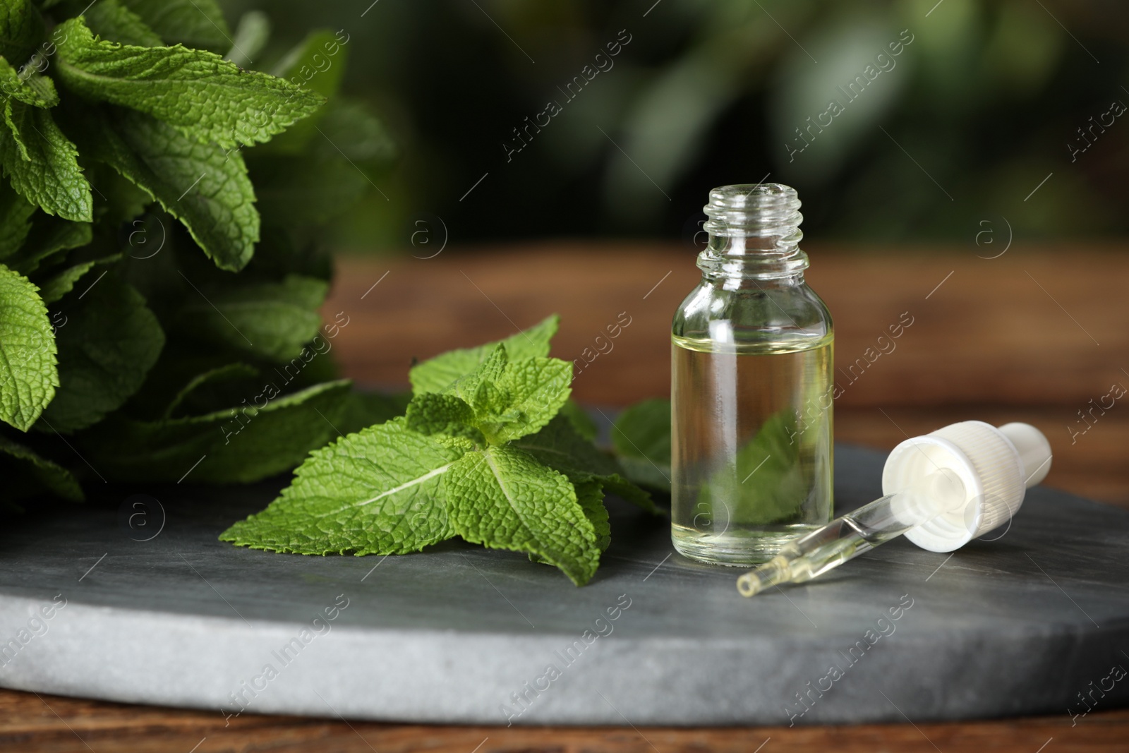 Photo of Bottle of mint essential oil, pipette and green leaves on wooden table, closeup