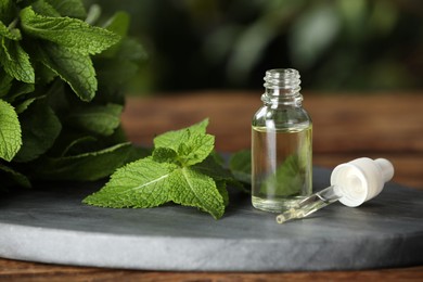 Bottle of mint essential oil, pipette and green leaves on wooden table, closeup