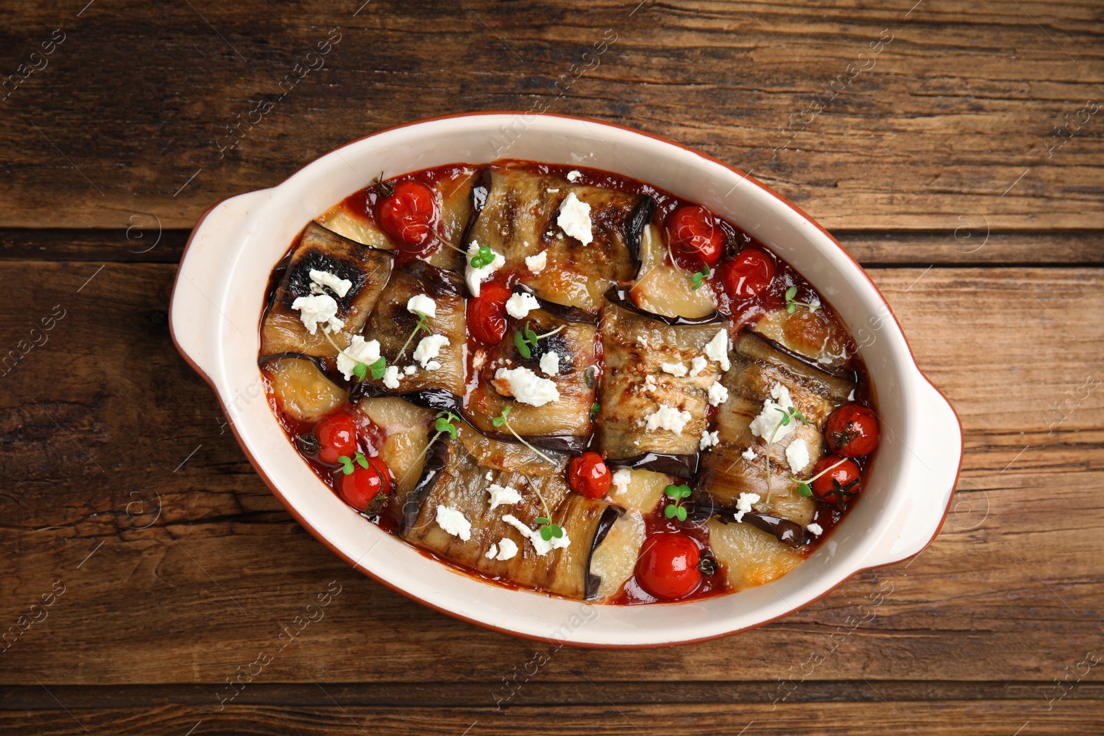 Photo of Tasty eggplant rolls with tomatoes, cheese and microgreens in baking dish on wooden table, top view