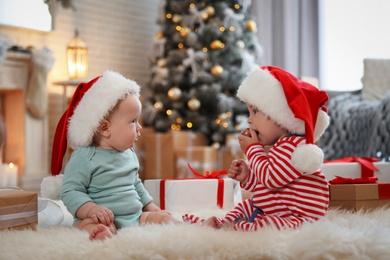 Cute children in Santa hats on floor in room with Christmas tree