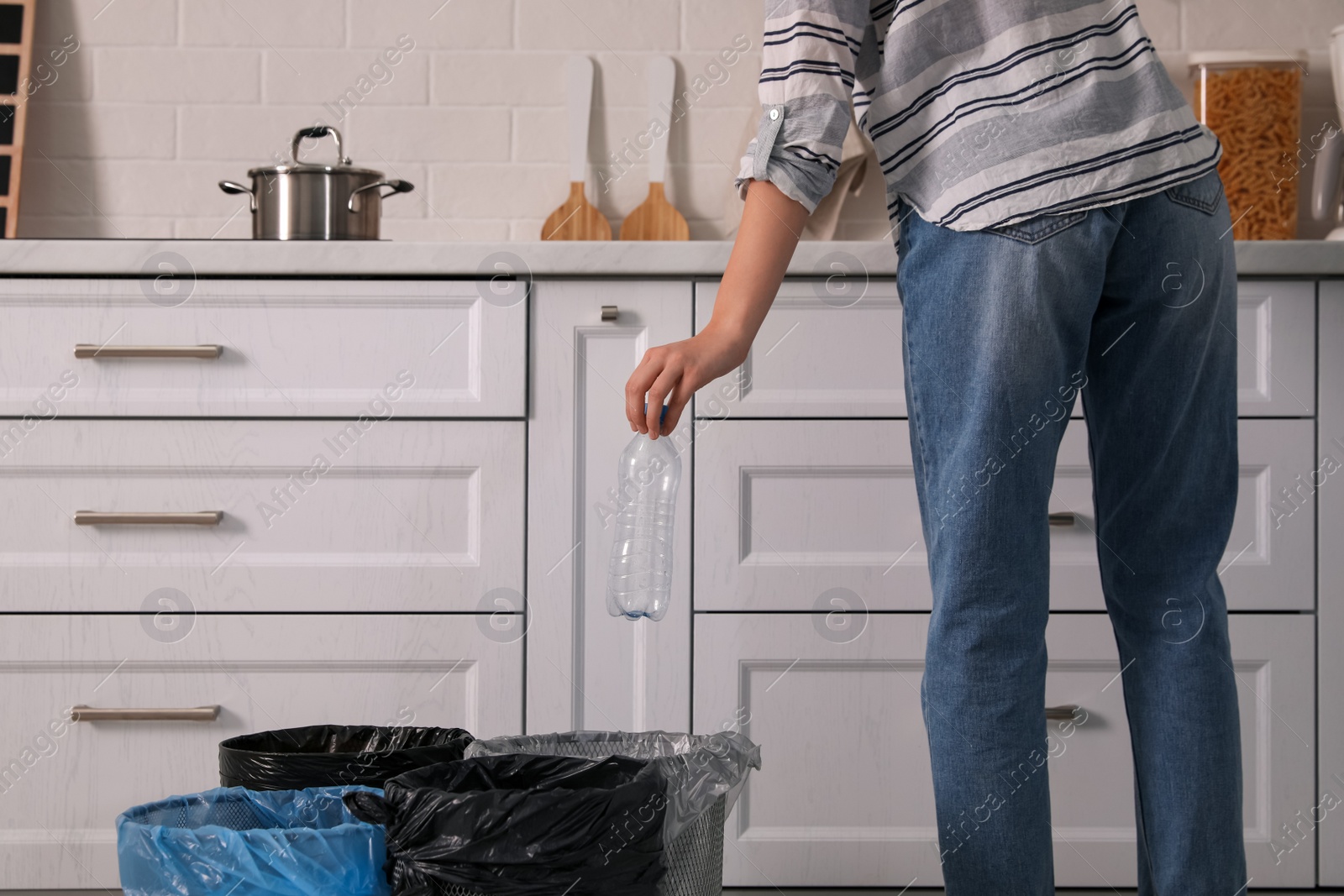 Photo of Woman throwing plastic bottle into trash bin in kitchen, closeup. Separate waste collection